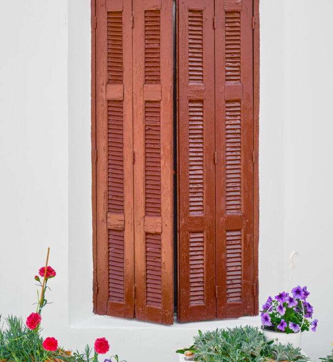 Wooden shutters and flower pots in front of an old traditional house in the city of Lindos on the island of Rhodes, the Greek islands of the Dodecanese archipelago, a popular tourism destination